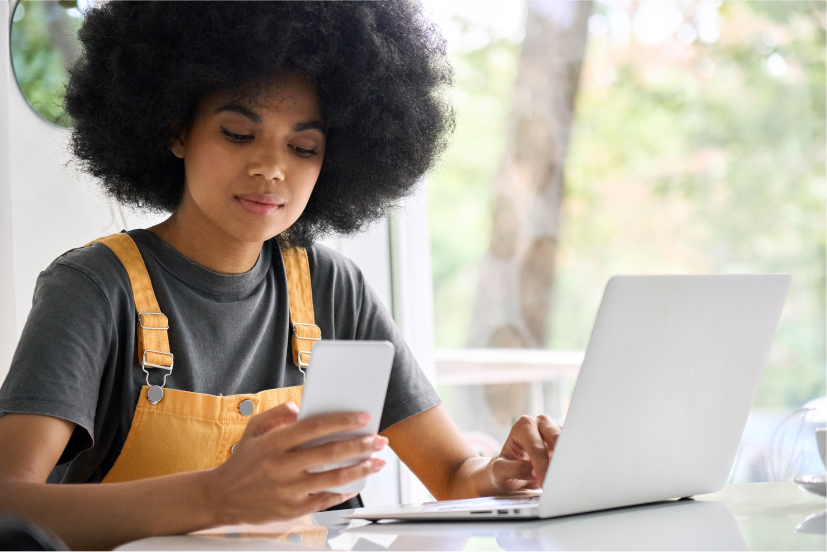 Woman sitting at a table using a mobile phone and laptop