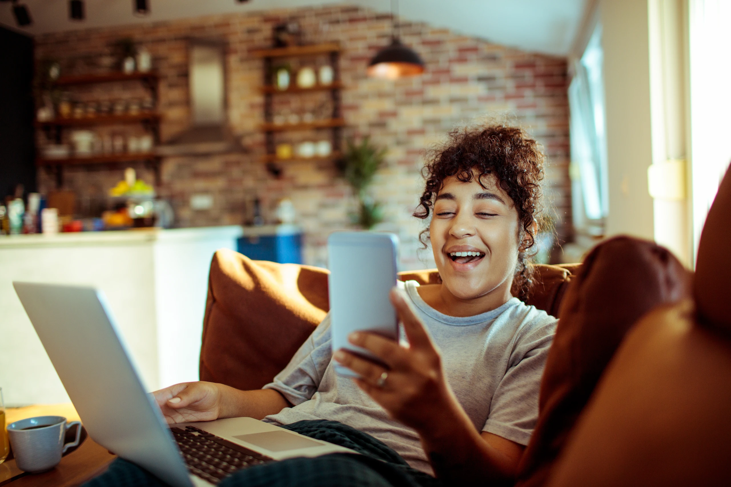 Leadspace Woman sitting on a couch looking at a mobile phone while using a laptop