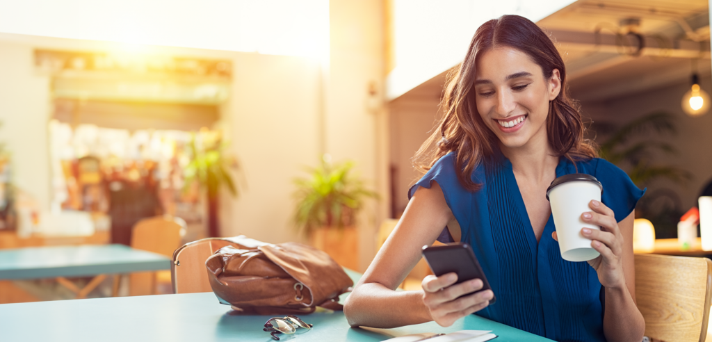 Woman engaged with cell phone smiling and holding coffee