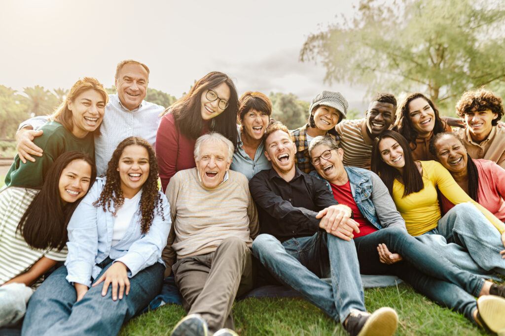 A group of people of all demographics sitting on the grass, laughing and smiling.